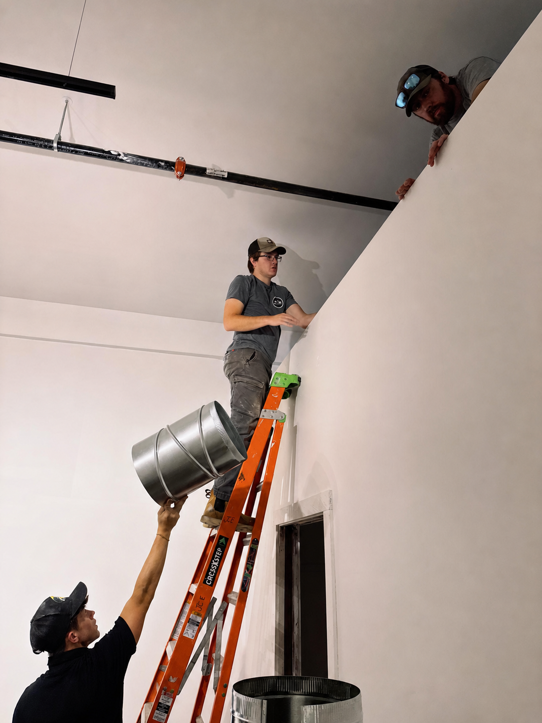 Technician handing a metal duct fitting to another technician on a ladder